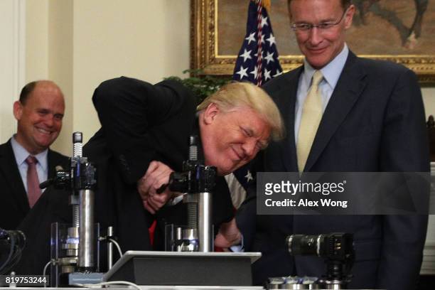 President Donald Trump tries to break a medicine bottle with a press as Corning CEO Wendell Weeks and Rep. Tom Reed look on during an announcement...