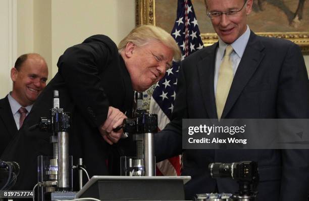 President Donald Trump tries to break a medicine bottle with a press as Corning CEO Wendell Weeks and Rep. Tom Reed look on during an announcement...