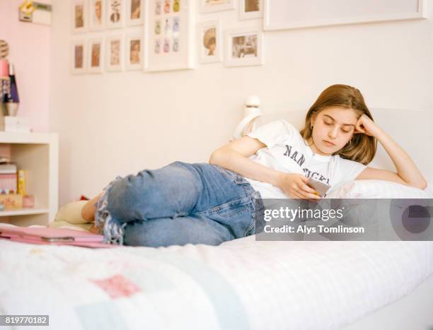 teenage girl lying on bed, using mobile phone - girl in her bed stockfoto's en -beelden