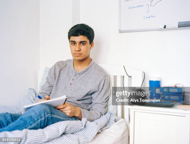 portrait of teenage boy sitting on bed and studying - boy sitting on bed stock-fotos und bilder