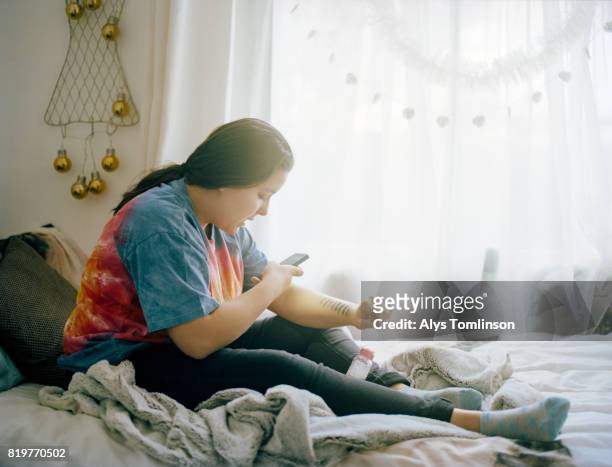 teenage girl sitting on bed, taking photograph of herself - plump girls stockfoto's en -beelden