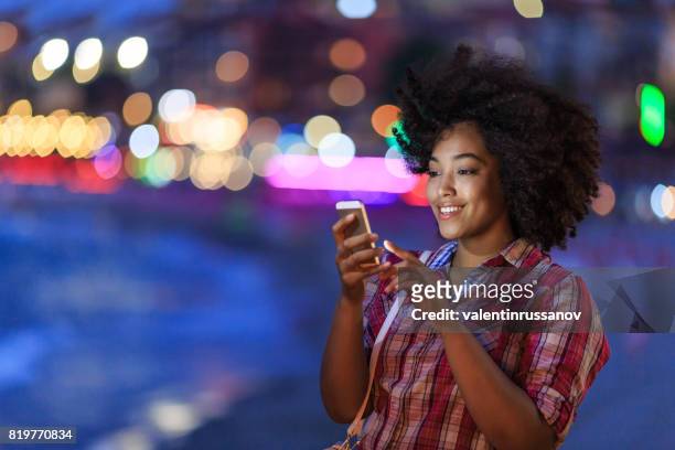 smiling tourist using smart phone at night on street - smartphones dangling stock pictures, royalty-free photos & images