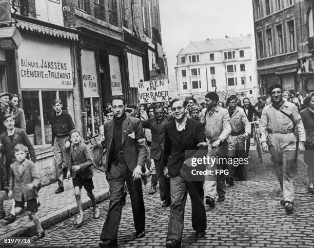 Nazi collaborator is marched through the streets of Louvain in liberated Belgium by the Armee Blanche , holding a sign in Flemish which reads 'Ik ben...