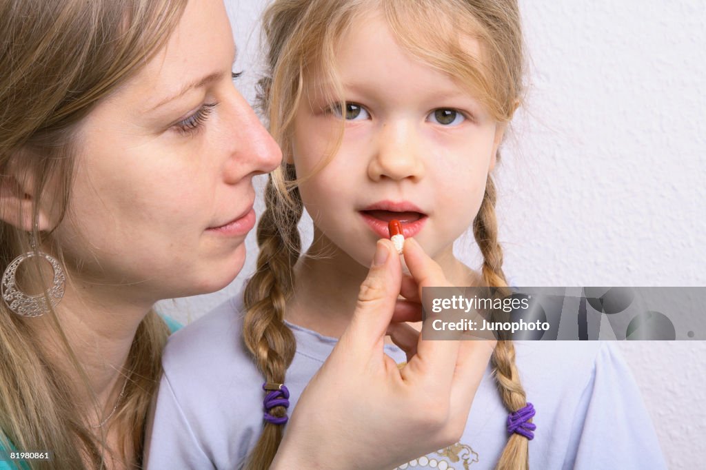 A mother giving her daughter a pill