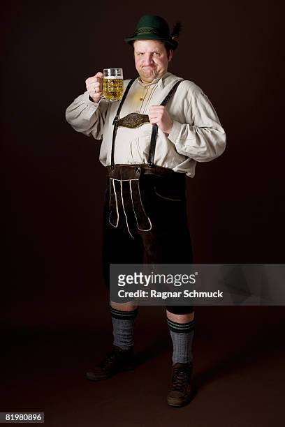 stereotypical german man in bavarian costume raising a beer in toast - hose aus leder stock-fotos und bilder