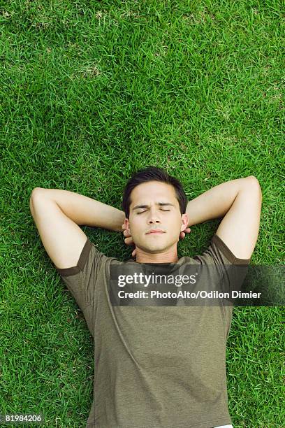 young man lying on grass with hands behind head, eyes closed, high angle view - hands behind head stock pictures, royalty-free photos & images