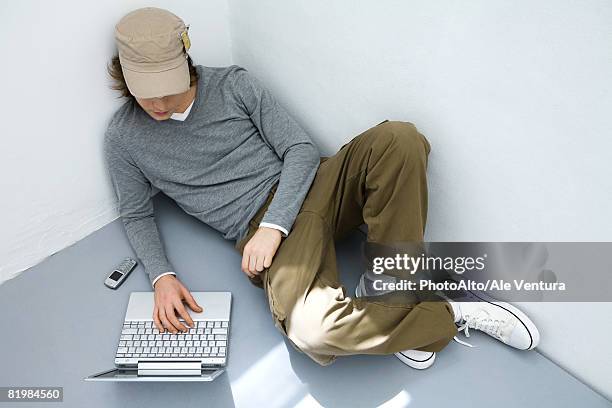 young man sitting on the ground, using laptop computer, high angle view - mala postura fotografías e imágenes de stock