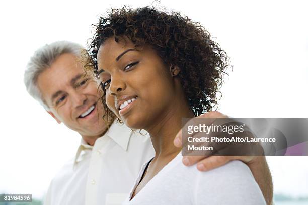 man with arm around woman's shoulder, woman smiling at camera, side view - age contrast stock pictures, royalty-free photos & images