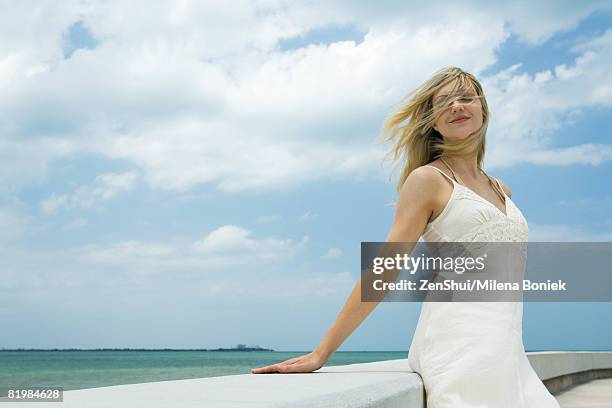 young woman leaning against ledge with eyes closed, wind blowing hair over face, smiling - underklänning bildbanksfoton och bilder