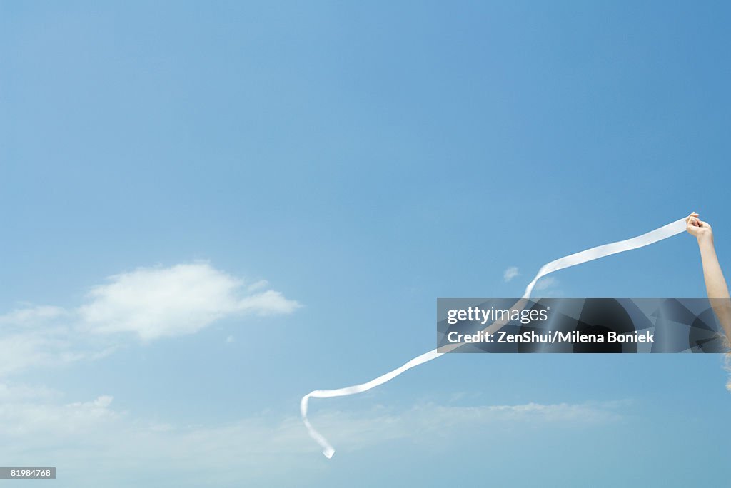 Woman holding up streamer against blue sky, cropped view