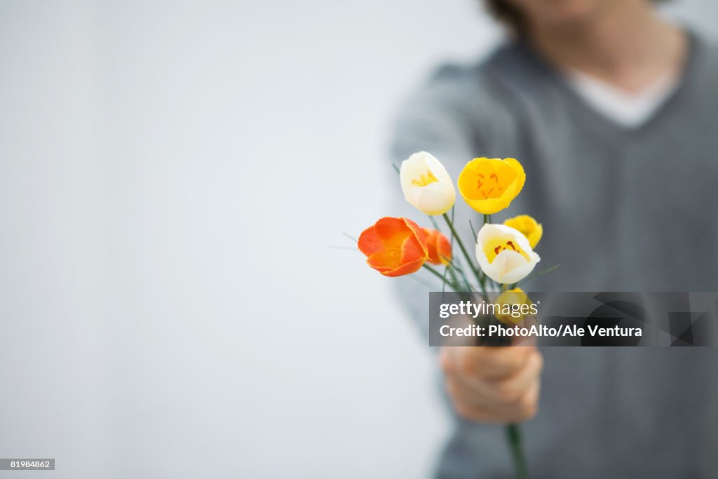 Man holding tulips out toward camera, cropped view, focus on foreground
