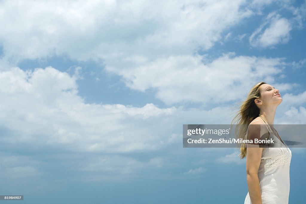 Young woman standing outdoors with head back, eyes closed, side view, low angle