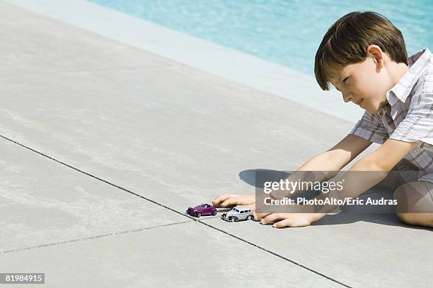 boy sitting on the ground next to swimming pool, playing with cars, cropped view - boy squinting stock pictures, royalty-free photos & images