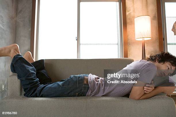 young man lying down on sofa, mid section, side view - auf dem bauch liegen stock-fotos und bilder