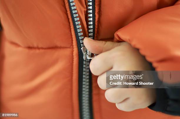 child pulling zip on orange jacket, close up - reißverschluß stock-fotos und bilder