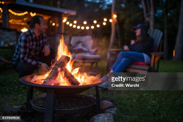 jong gezin is opwarming van de aarde in de buurt van kampvuur late avond bij een mooie canadese chalet - camping at night stockfoto's en -beelden