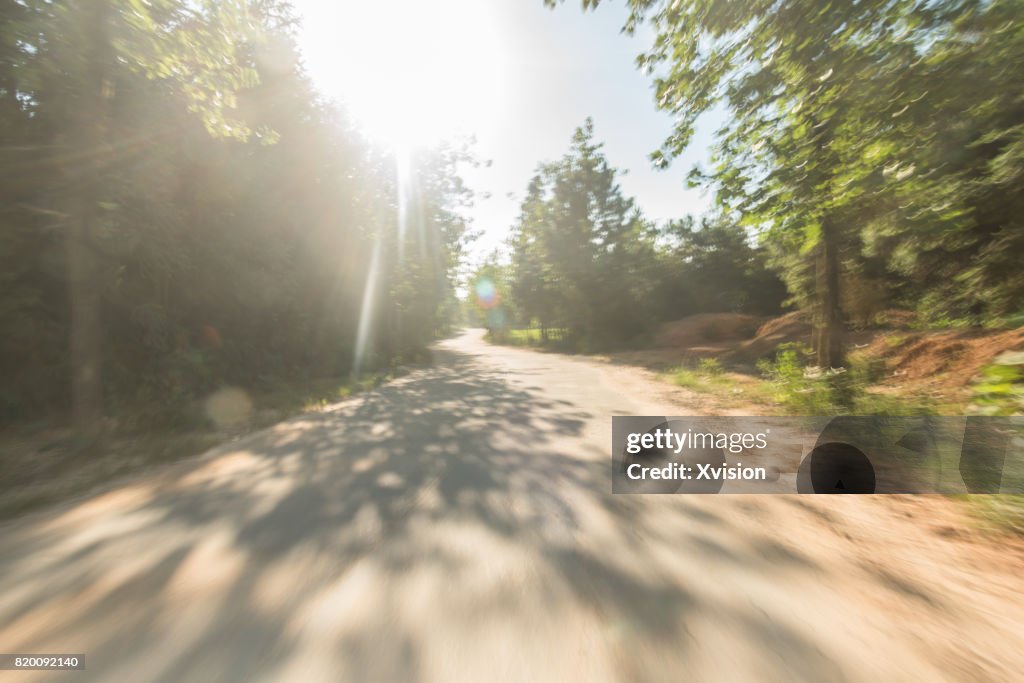 Concrete road under blue sky with clouds in motion blur with plants in sides