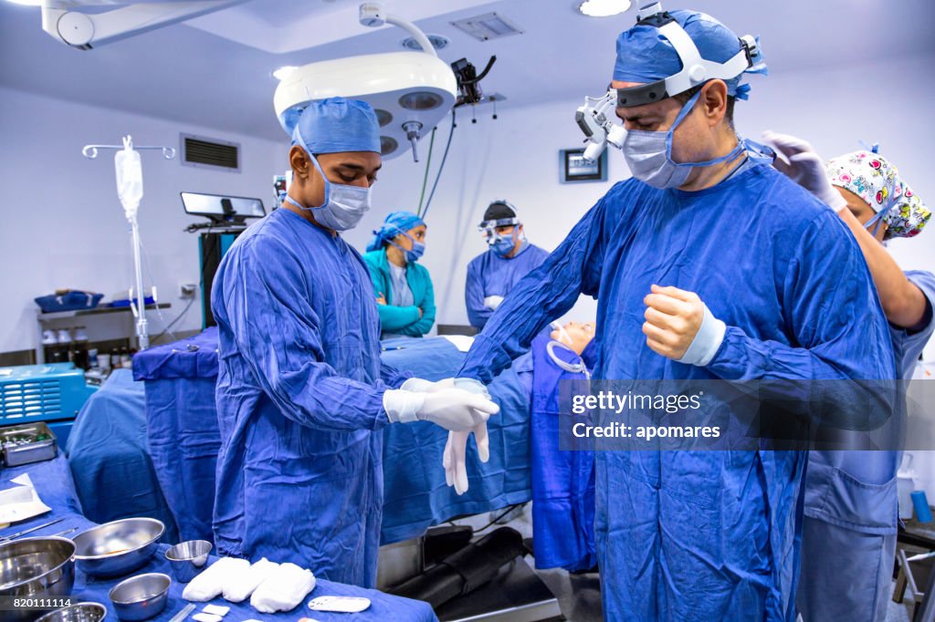 Surgeon getting ready for surgical procedure. Assistant helping set surgical gloves.