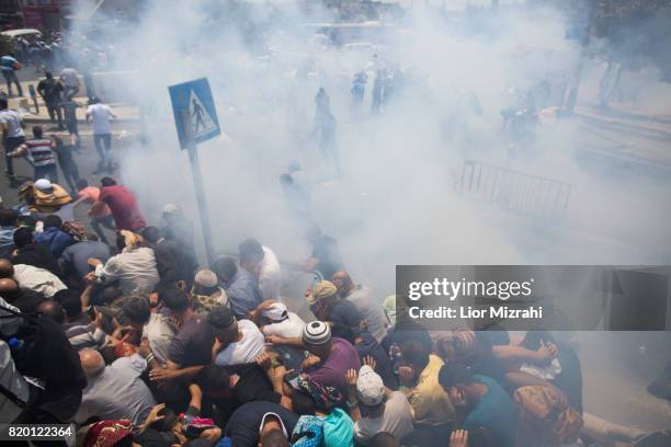 Palestinian worshippers run for cover from teargas, fired by Israeli forces, following prayers in Ras el-Amud Area outside the Old City on July 21,...