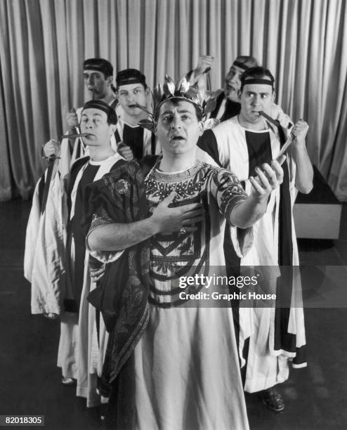 American comic actor Sid Caesar as Julius Caesar, circa 1952. Lurking behind him is a group of dagger-wielding and cigar-smoking senators, including...