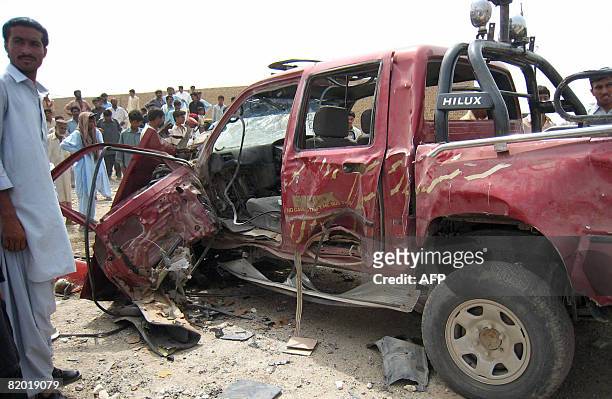 Pakistani people gather around a damaged vehicle hit by a road side blast at Dera Bugti district in southwestern Baluchistan province on July 21,...