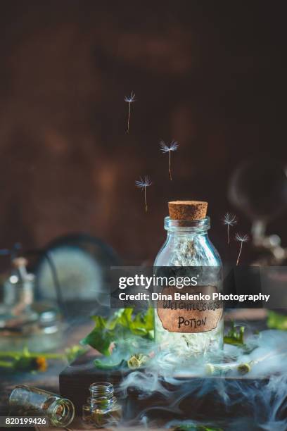 glass potion bottle with dandelion seeds and handcrafted label in a magical still life with smoke - green potion stock pictures, royalty-free photos & images