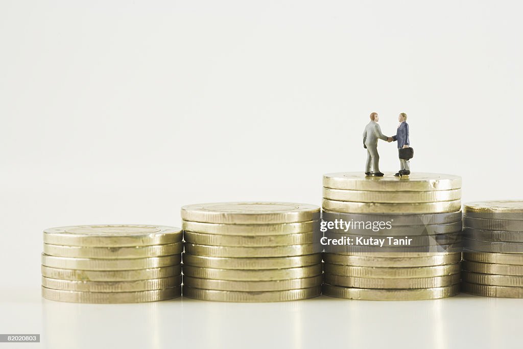 Businessmen figurines shaking hands on stacks of golden coins. (focus on figurines)