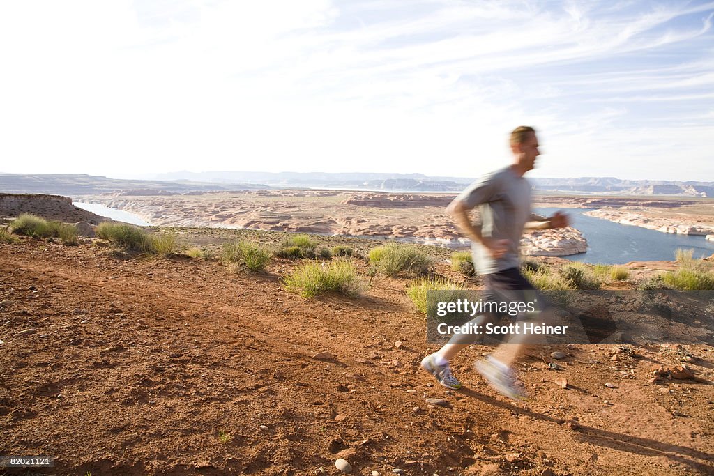 A male runner runs the rim of Lake Powell. Runner is out of focus to indicate movement.