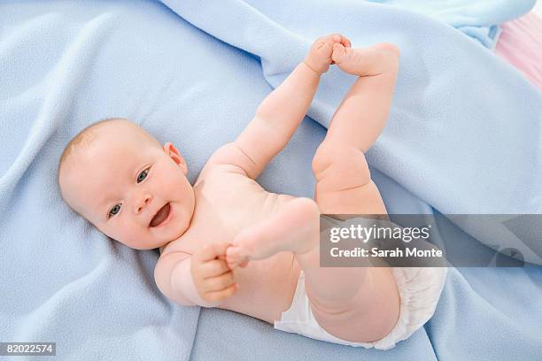 baby boy (6-9 months) lying on bed, touching toes - zehenspitzen berühren stock-fotos und bilder