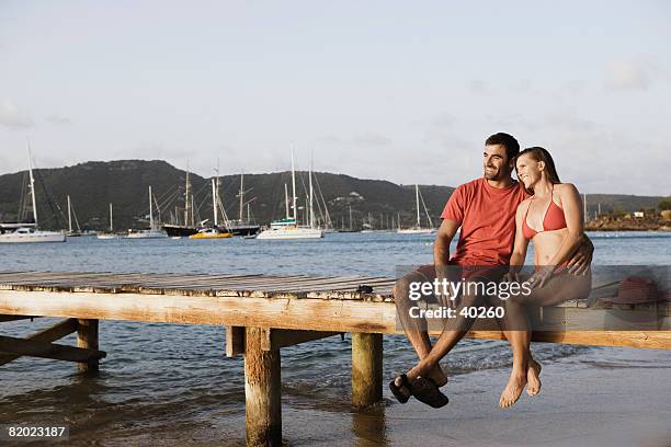 mid adult man with his arm around a mid adult woman and sitting on a jetty - ankle boot stockfoto's en -beelden