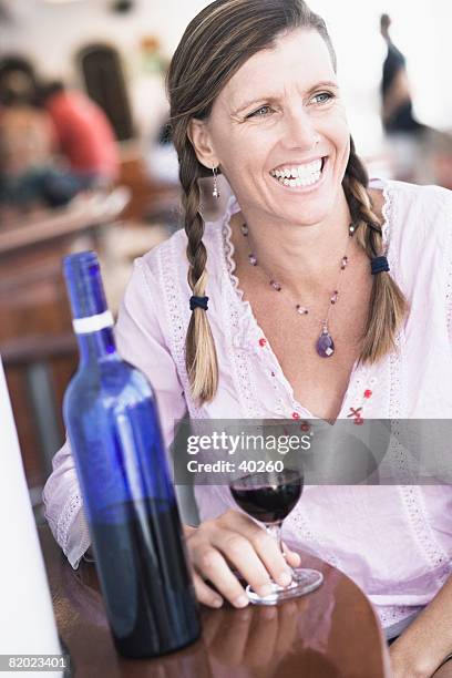 mid adult woman sitting at a table and holding a glass of wine - wine bottle transport stock pictures, royalty-free photos & images