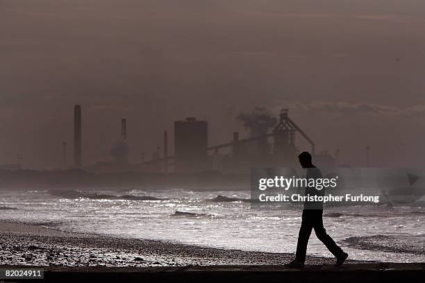 Man walks along Redcar beach at high tide in the shadow of the Corus Steelworks in Teeside, on July 21 in Middlesborough, England. The giant iron and...