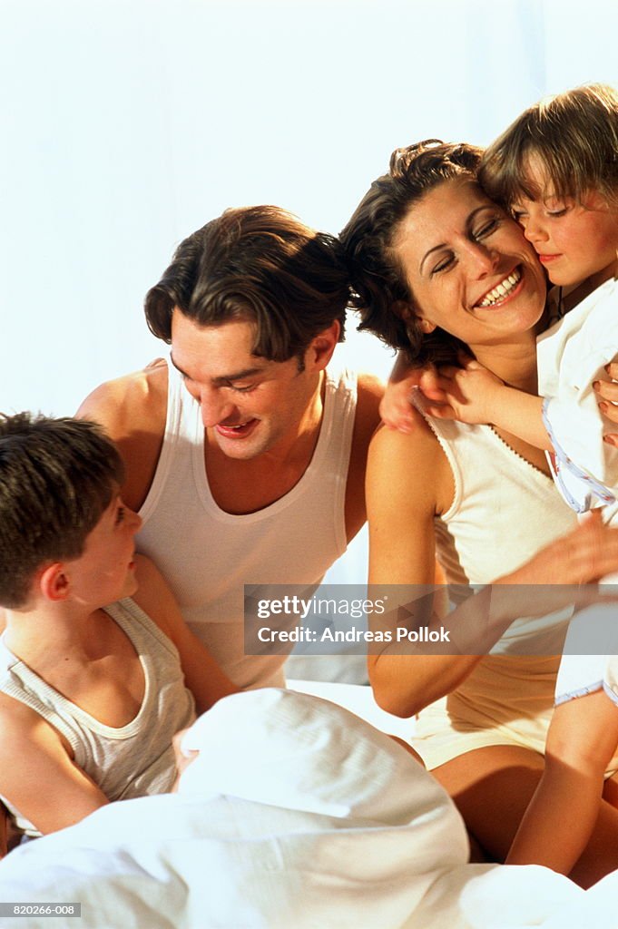 Parents sitting on bed with son and daughter (4-6), portrait