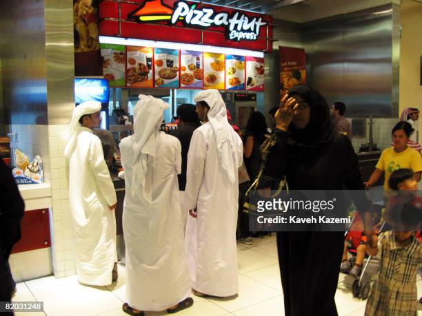 Emirati men in their traditional white dish dash wait to order food at a Pizza Hut stand in the food court in the Mall of Emirates in Dubai city on 9...