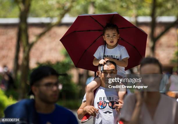 Young girl is shielded from the sun with an umbrella as a family walks through Battery Park in Lower Manhattan, July 21, 2017 in New York City....