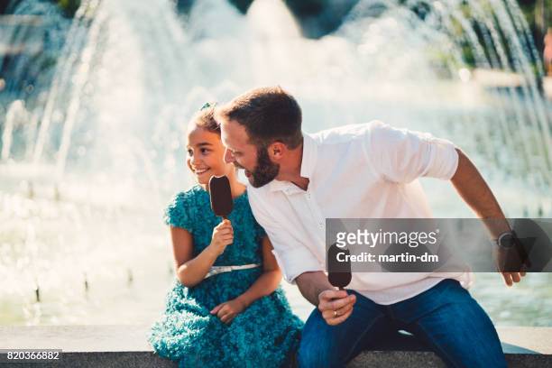 alleenstaande vader en dochter eten van ijs bij de fontein - chocoladeijs stockfoto's en -beelden