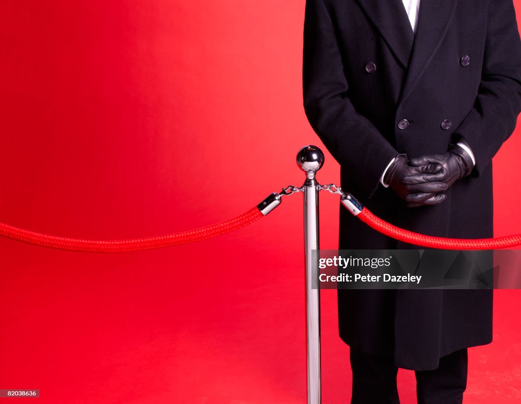 Doorman at red carpet event guarding entrance.