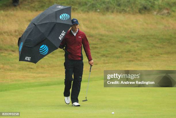 Jordan Spieth of the United States shelters from the rain under an umbrella on the 18th green during the second round of the 146th Open Championship...