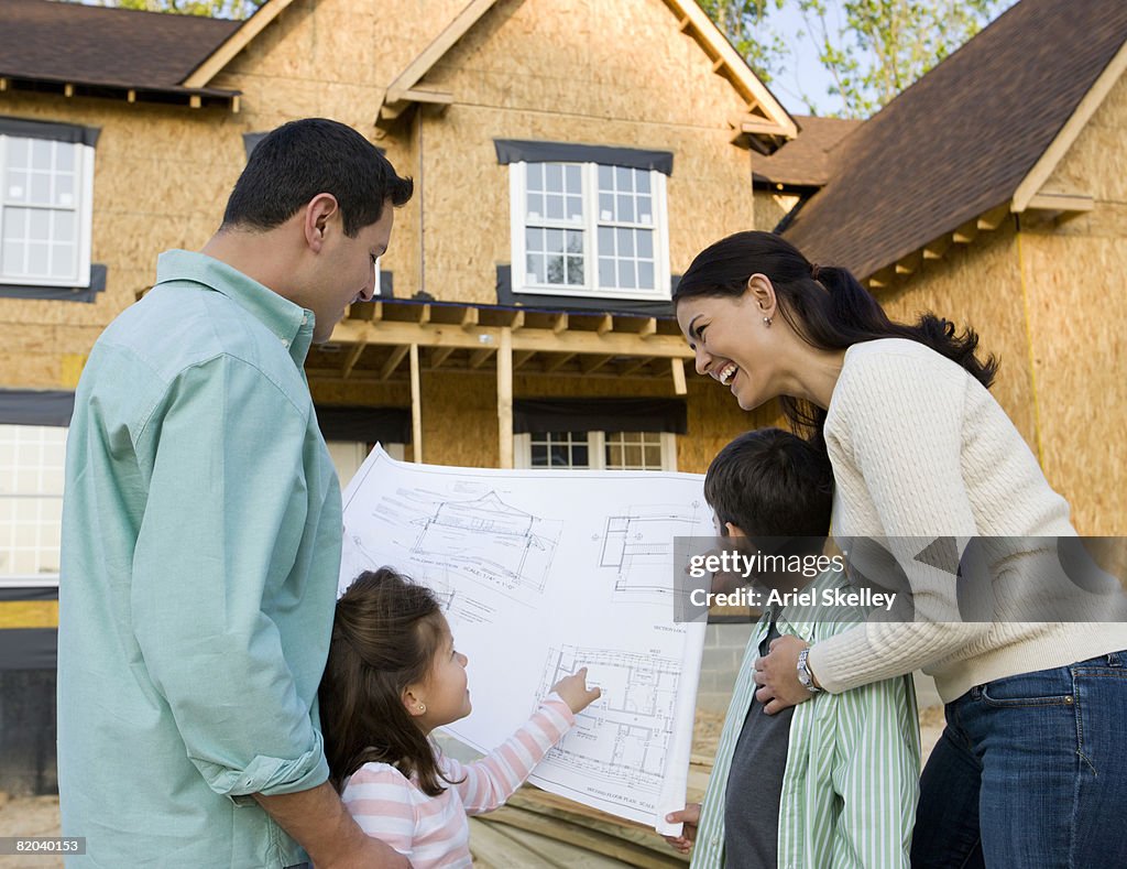 Young Family in Front of New Home Under Construction with Blueprints