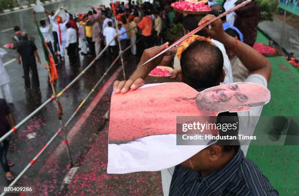 Supporters huddle under cutout of BJP National President Amit Shah during sudden showers while waiting to welcome him on his way in a procession from...
