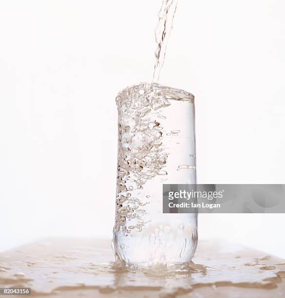 one glass being overfilled with water. - filling imagens e fotografias de stock