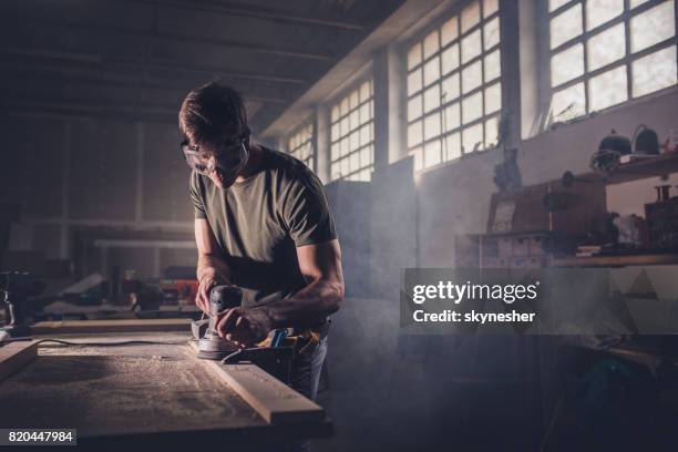 mannelijke timmerman met behulp van sander op een stuk hout in een houtklas schooljaar. - elektrisch gereedschap stockfoto's en -beelden