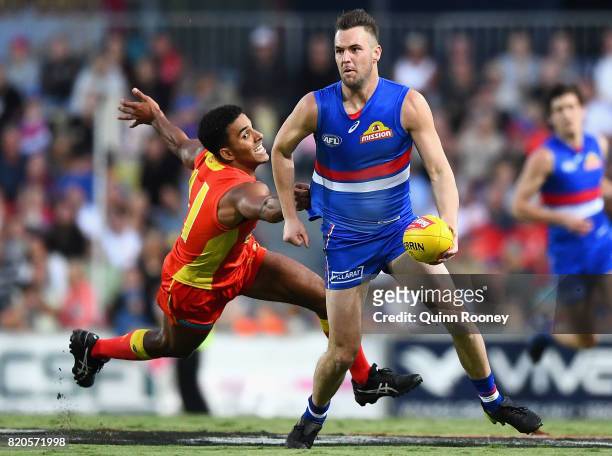 Matthew Suckling of the Bulldogs handballs whilst being tackled by Touk Miller of the Suns during the round 18 AFL match between the Western Bulldogs...