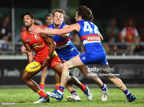 Aaron Hall of the Suns handballs whilst being tackled by Jackson Macrae and Liam Picken of the Bulldogs during the round 18 AFL match between the...