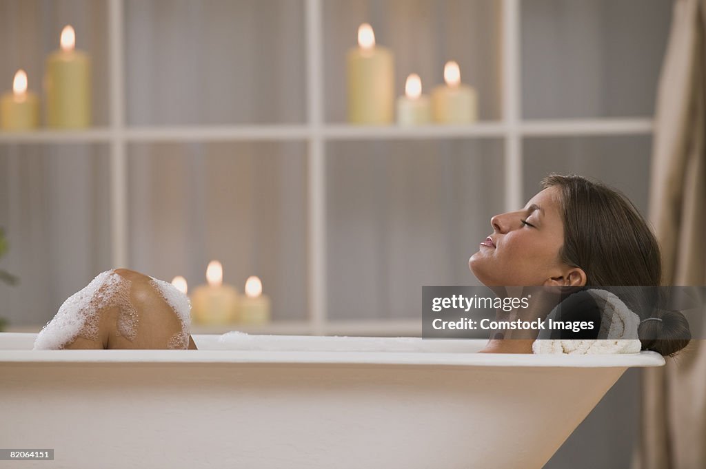 Content woman lying in bathtub with candles
