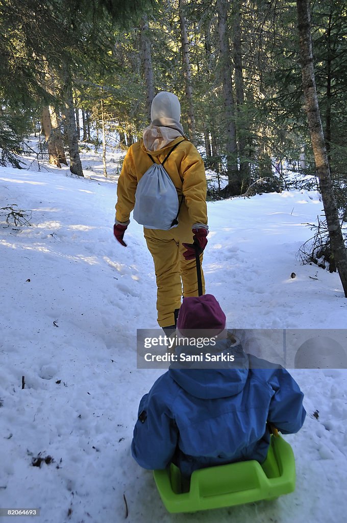 Mother pulling daughter  (7-8)  in sled in forest, French Alps, France