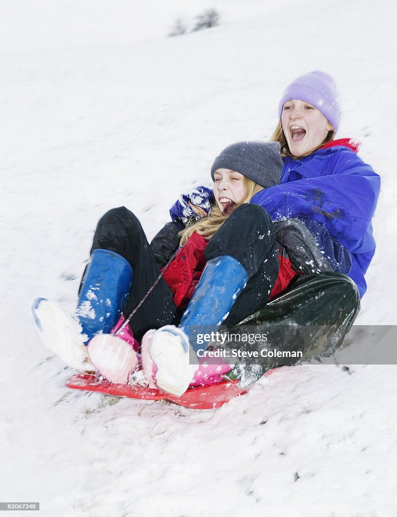 Two teenage girls, 13 years and 14 years old, sliding down hill on sledge