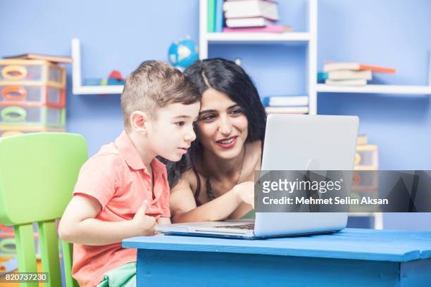 mixed race nanny and little boy using computer in preschool room - nanny smiling stockfoto's en -beelden