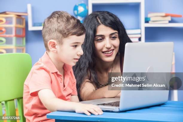 mixed race nanny and little boy using computer in preschool room - nanny smiling stockfoto's en -beelden