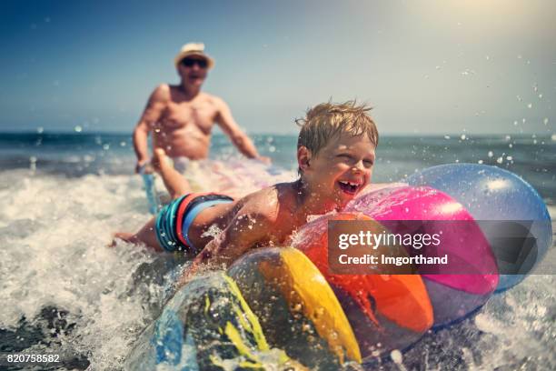 kleiner junge mit großvater spielen in den wellen des meeres - candid beach stock-fotos und bilder